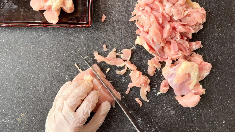 Thinly slicing partially frozen chicken thighs on cutting board wearing gloves