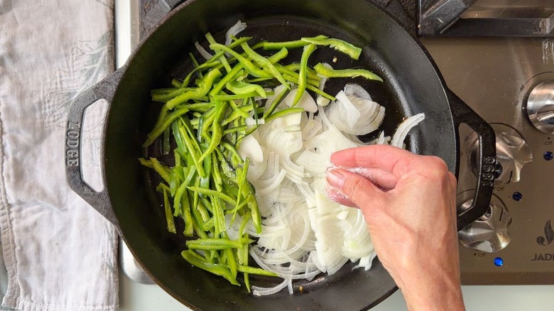 Salting sliced poblano pepper and sweet onion in cast iron skillet on stovetop