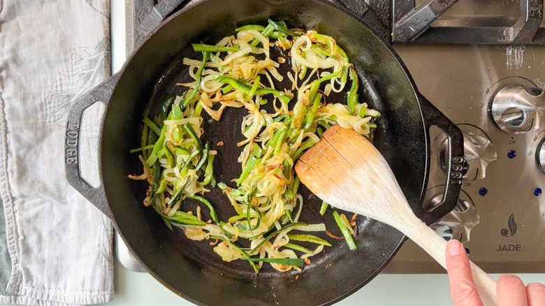 Sauteeing caramelized poblano pepper and sweet onion slices in cast iron skillet with wooden spoon
