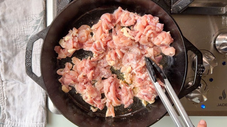 Thinly sliced raw chicken thighs in cast iron skillet on stovetop