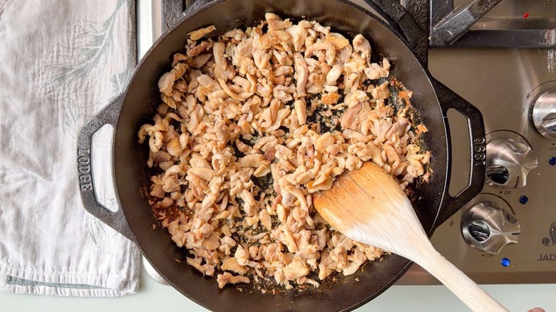 Sauteeing chopped chicken thighs in cast iron skillet with wooden spoon