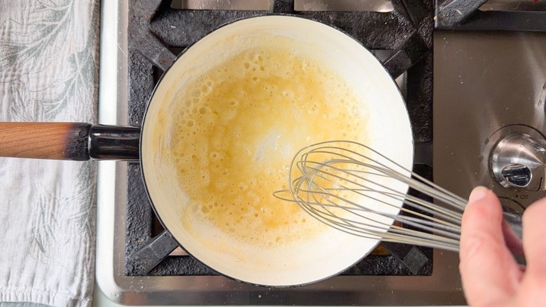 Whisking flour into melted butter in saucepan on stovetop