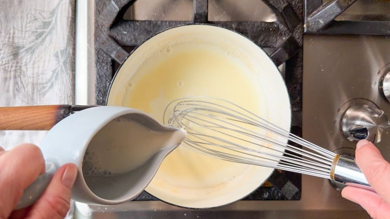 Pouring milk into roux in saucepan on stovetop