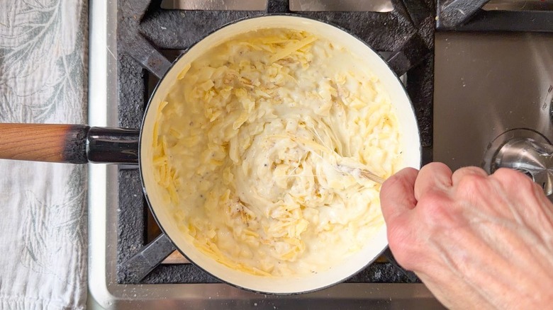 Stirring shredded cheeses into a cheese sauce in a saucepan with a wooden spoon