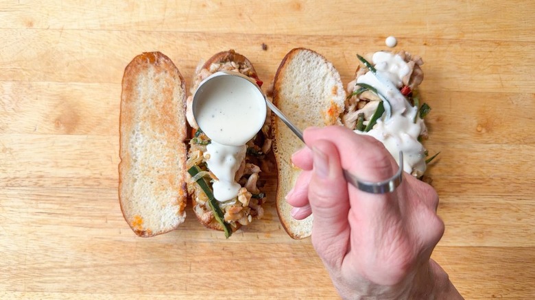 Adding cheese sauce to chicken cheesesteak sandwiches with small ladle