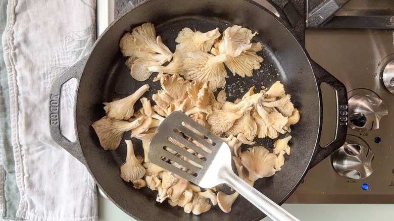 Pressing down on oyster mushrooms in cast iron skillet with metal spatula on stovetop