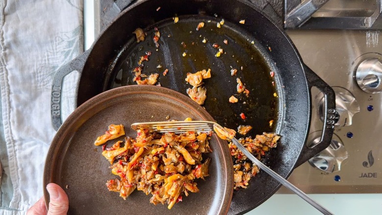 Transferring oyster mushroom relish from cast iron skillet to plate using metal spatula
