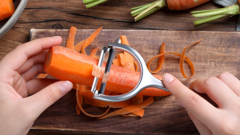 hands peeling a carrot with a peeler over cutting board