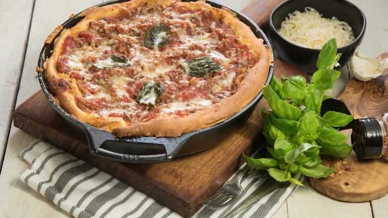 Deep dish pizza in a cast iron skillet with basil leaves on top