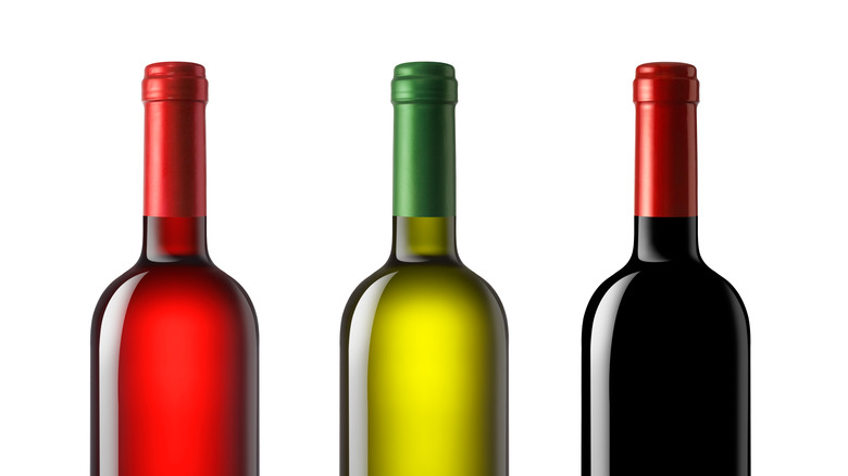Wine bottles of differing colors lined up in front of a white background