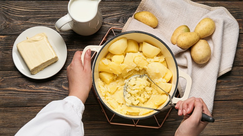 Hands preparing mashed potatoes with masher