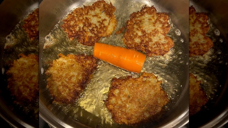 Carrot in the middle of a pan of oil with latkes frying around it