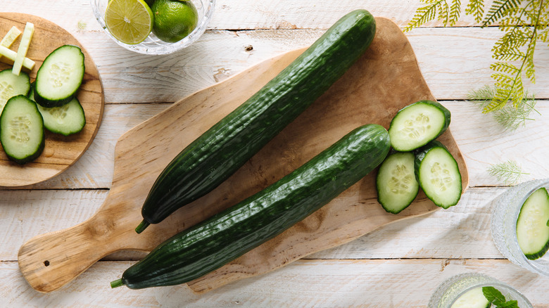 Whole and sliced English cucumbers on a wooden cutting board