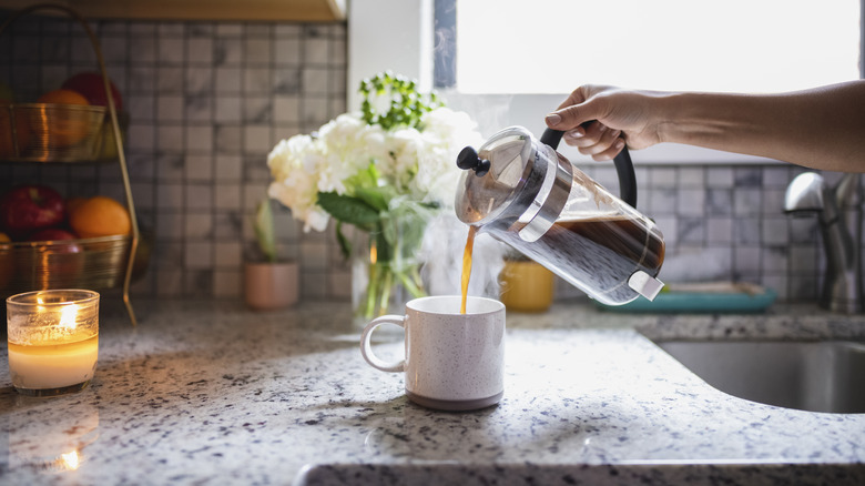A hand pouring coffee from a French press into a cup on a kitchen counter