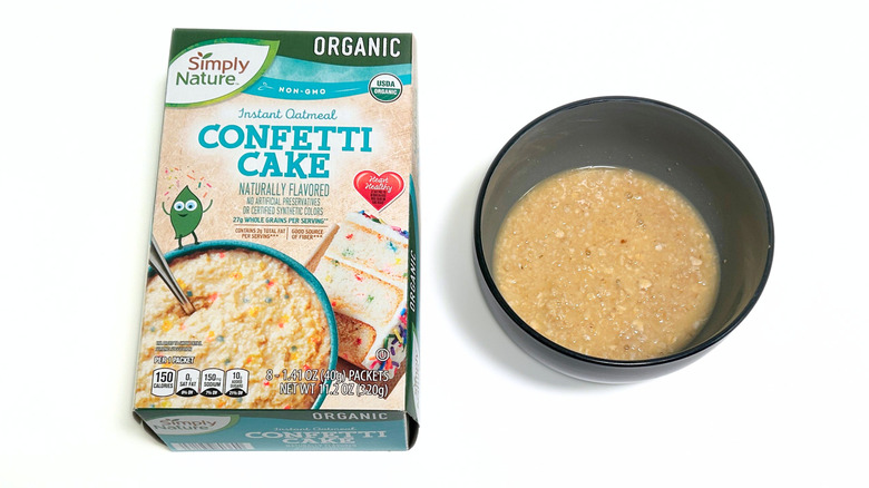 A box of Simply Nature Organic Confetti Cake Oatmeal next to a black bowl of oatmeal