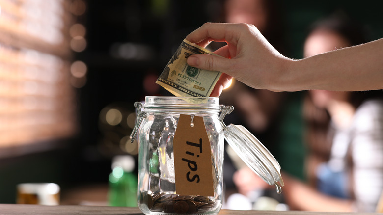 hand putting money in tip jar 