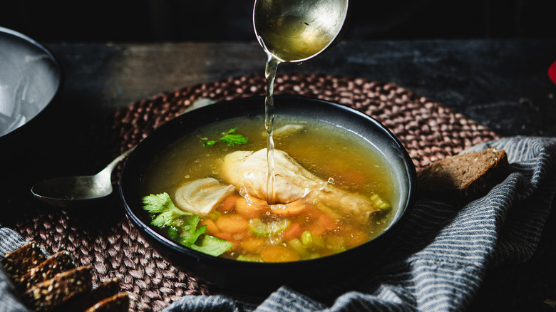 Ladle pouring chicken broth into bowl with chicken and vegetables
