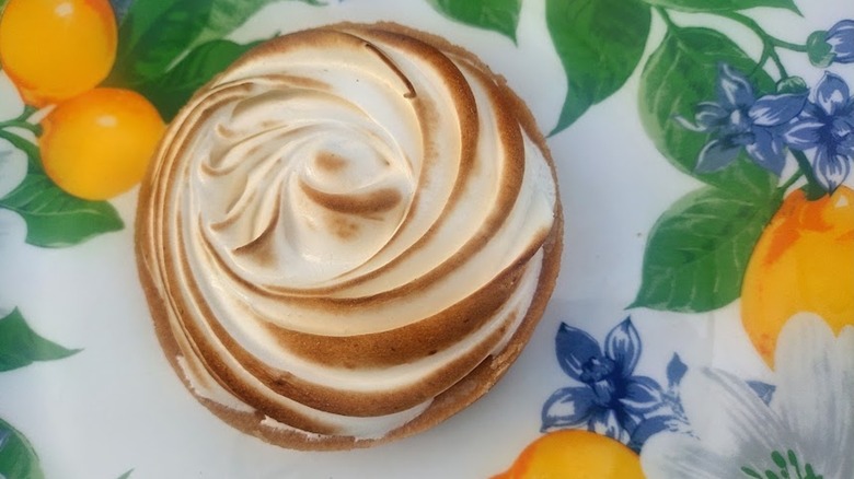 whole and half lemon meringue tartlets on a lemon-patterned plate