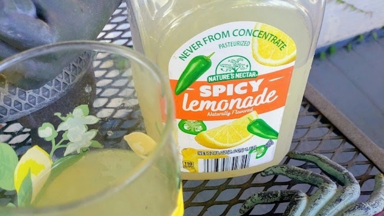 bottle and lemon-patterned glass of Nature's Nectar Spicy Lemonade sitting on a rustic wooden table in an outdoor setting