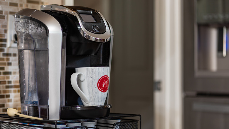 A black and silver coffee maker with a water basin and a white cup with a red 