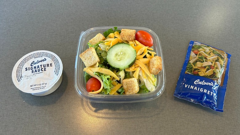 Side salad with croutons, cucumber, shredded cheese, and grape tomatoes in a plastic to-go cup with a side of Culver's Signature Sauce and Culver's Vinaigrette