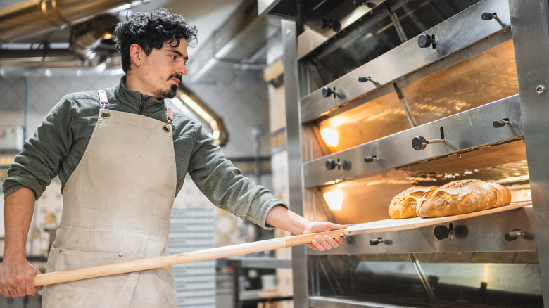 A baker taking freshly baked bread out of an oven