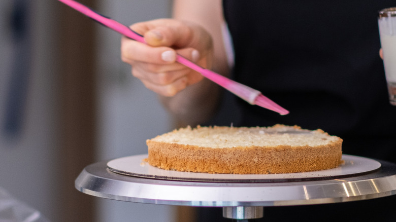 A baker brushing a cake with syrup before frosting it