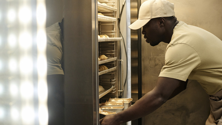 A chef placing a tray of baked goods in a freezer