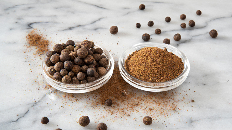 Close-up of dried Jamaican pepper (allspice) seeds and powder on a white marble background.