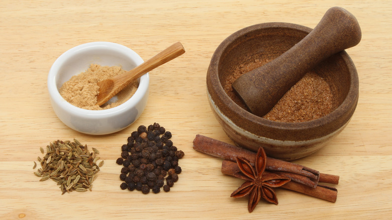 Ingredients for Chinese five spice with a ramekin and pestle and mortar on a wooden board