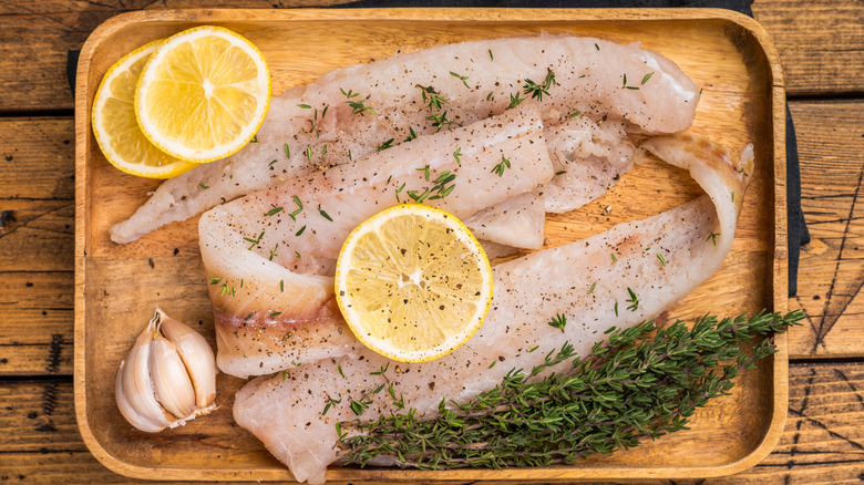 Raw catfish fillets on wooden tray with lemon and garnish