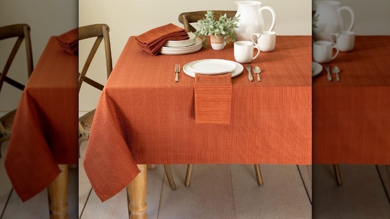 Orange textured tablecloth with placemats, plates, cups, and pitcher, and a plant