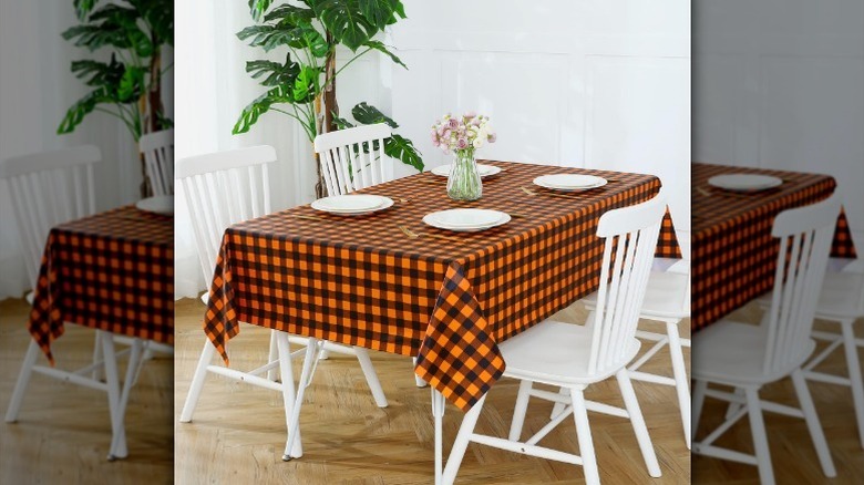Orange and black checkered tablecloth with white chairs and plates, and flowers