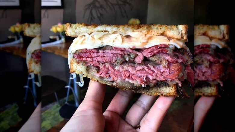 A hand holding half of a pastrami reuben up, with interior of the sandwich visible