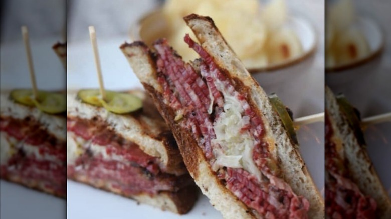 Close up of a pastrami sandwich with sauerkraut and topped with pickles held by toothpicks