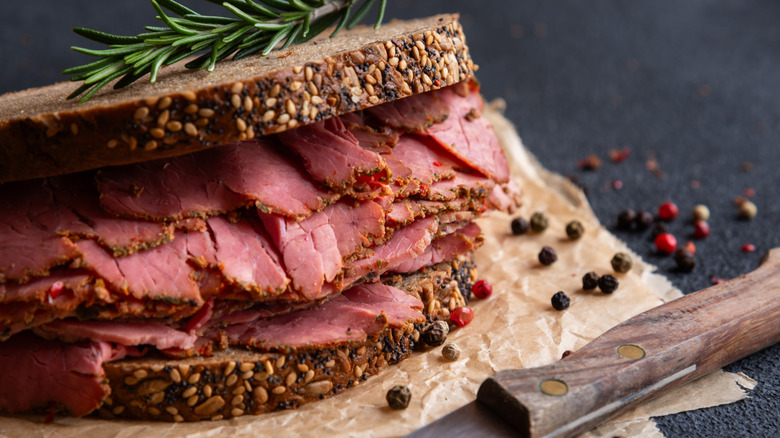 A pastrami sandwich on seeded bread presented on parchment paper with scattered peppercorns