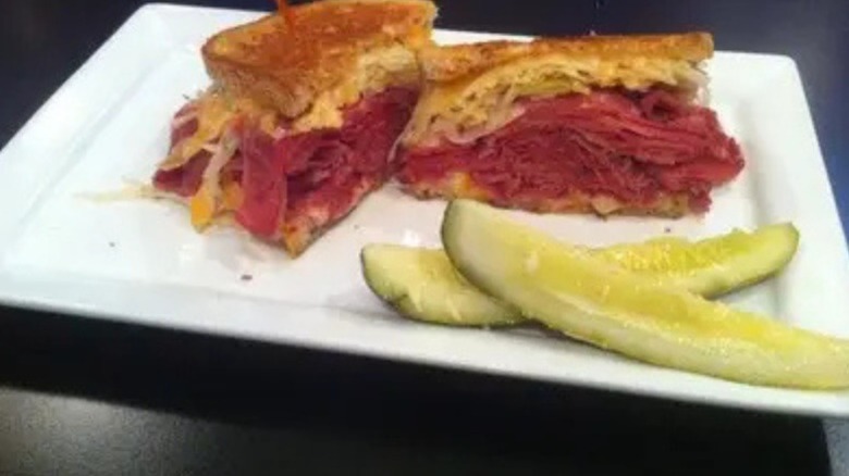 A reuben sandwich with a side pickle on a white plate