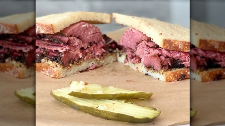 A pastrami sandwich cut in half and displayed on parchment paper