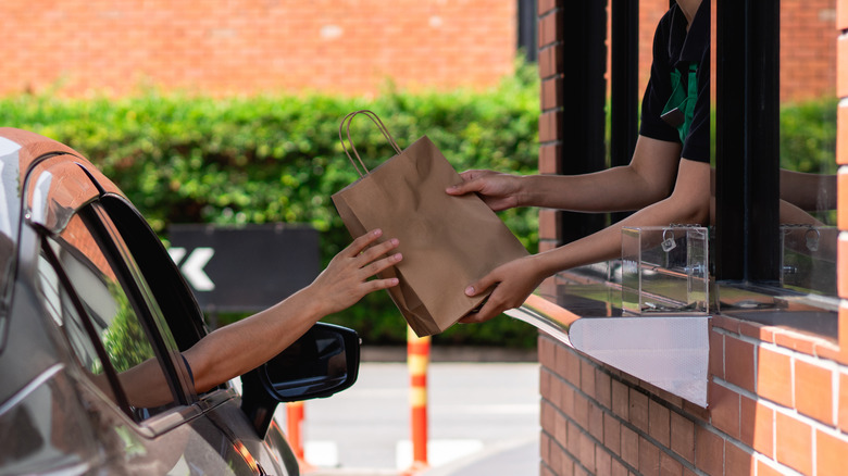 A worker handing a brown bag of food to a customer in a drive-thru