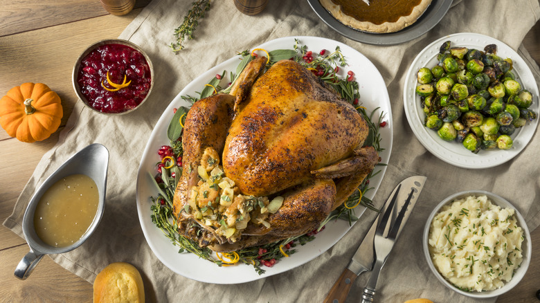 A whole roasted turkey stuffed with dressing and surrounded by sides in bowls