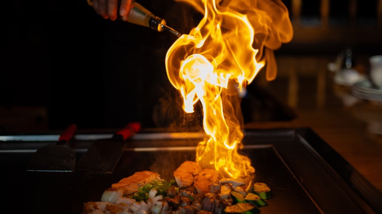 Fish and vegetables being cooked flambé on a restaurant hot plate