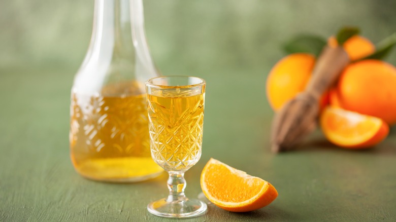 Glass and carafe of orange liqueur beside sliced oranges