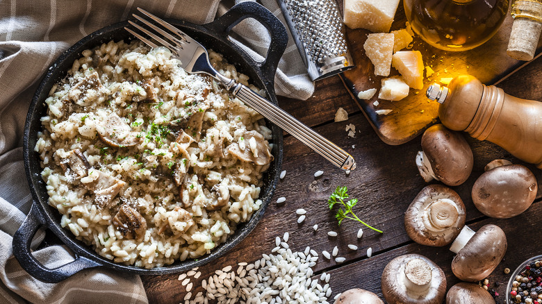 Italian risotto surrounded by raw rice, mushrooms, parsley, and parmesan cheese