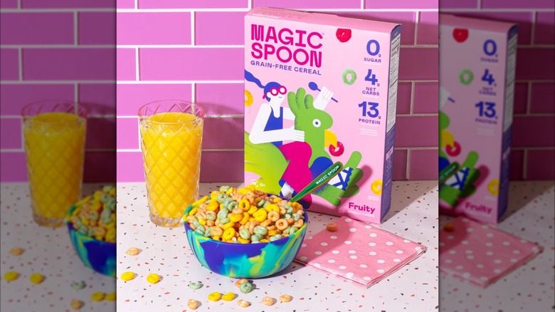 Fruity Magic Spoon cereal box and bowl with orange juice and pink background