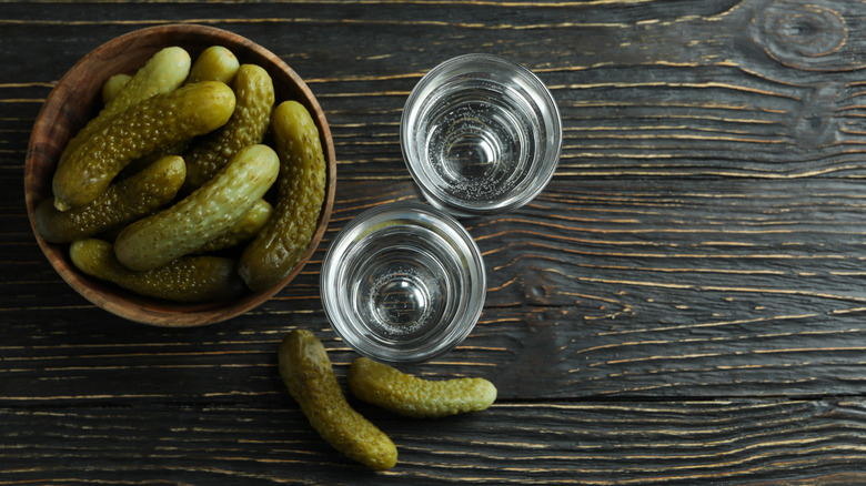 pickles in bowl next to shot glasses on wooden table