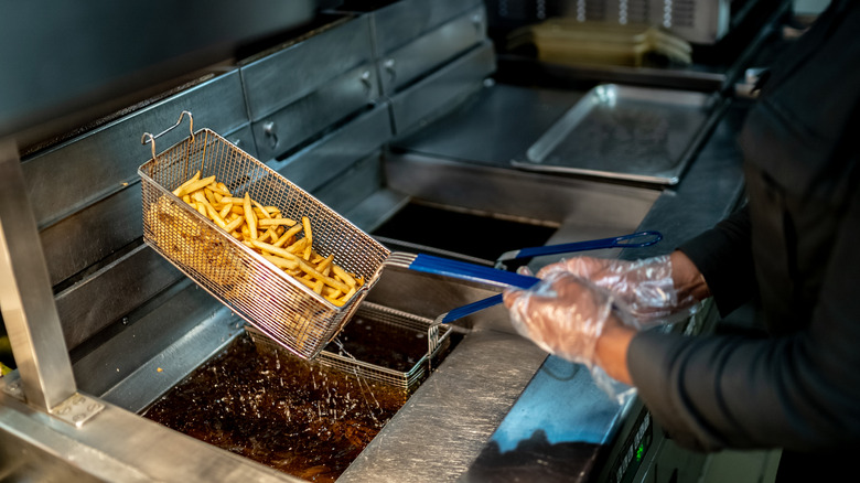 Worker holds fryer with fries at fast food restaurant