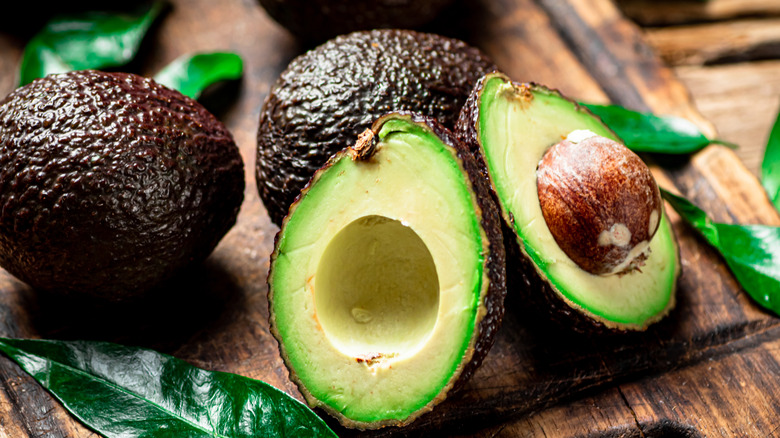 Avocado halves on a cutting board next to uncut avocados