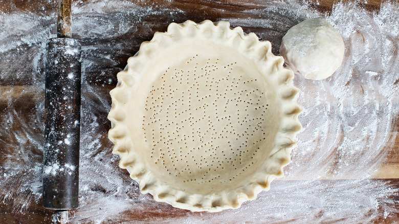 Homemade pie crust surrounded by flour with a rolling pin and ball of dough