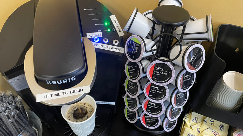 Black Keurig coffee maker brewing a cup and a stand full of coffee pods next to it.