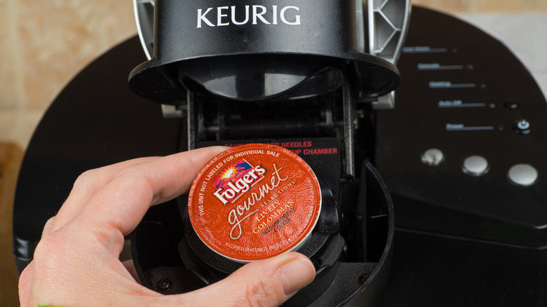 Hand putting a red "Folgers gourmet" coffee pod in a black Keurig Coffee Maker